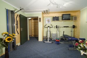 Ein Zimmer mit Laufband, Hantelbank und Fernseher auf einem Regal.