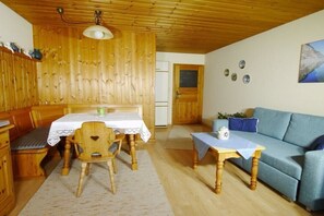 Ein Holzinnenraum mit einem Esstisch, Stühlen, einer Couch und einem kleinen Tisch mit einer Lampe.
