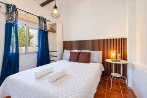 A hotel room with a bed, a bedside table with a lamp, and a window with curtains. - Countryside Escape Just Minutes from the Coast (Mijas)