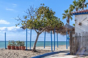 A beach scene with a tree, a thatched structure, and a building with a tiled roof. - Countryside Escape Just Minutes from the Coast (Mijas)