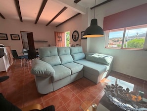 A living room with a sectional sofa, a dining table with chairs, a large window with a view, and a hanging pendant light. - Countryside Escape Just Minutes from the Coast (Mijas)