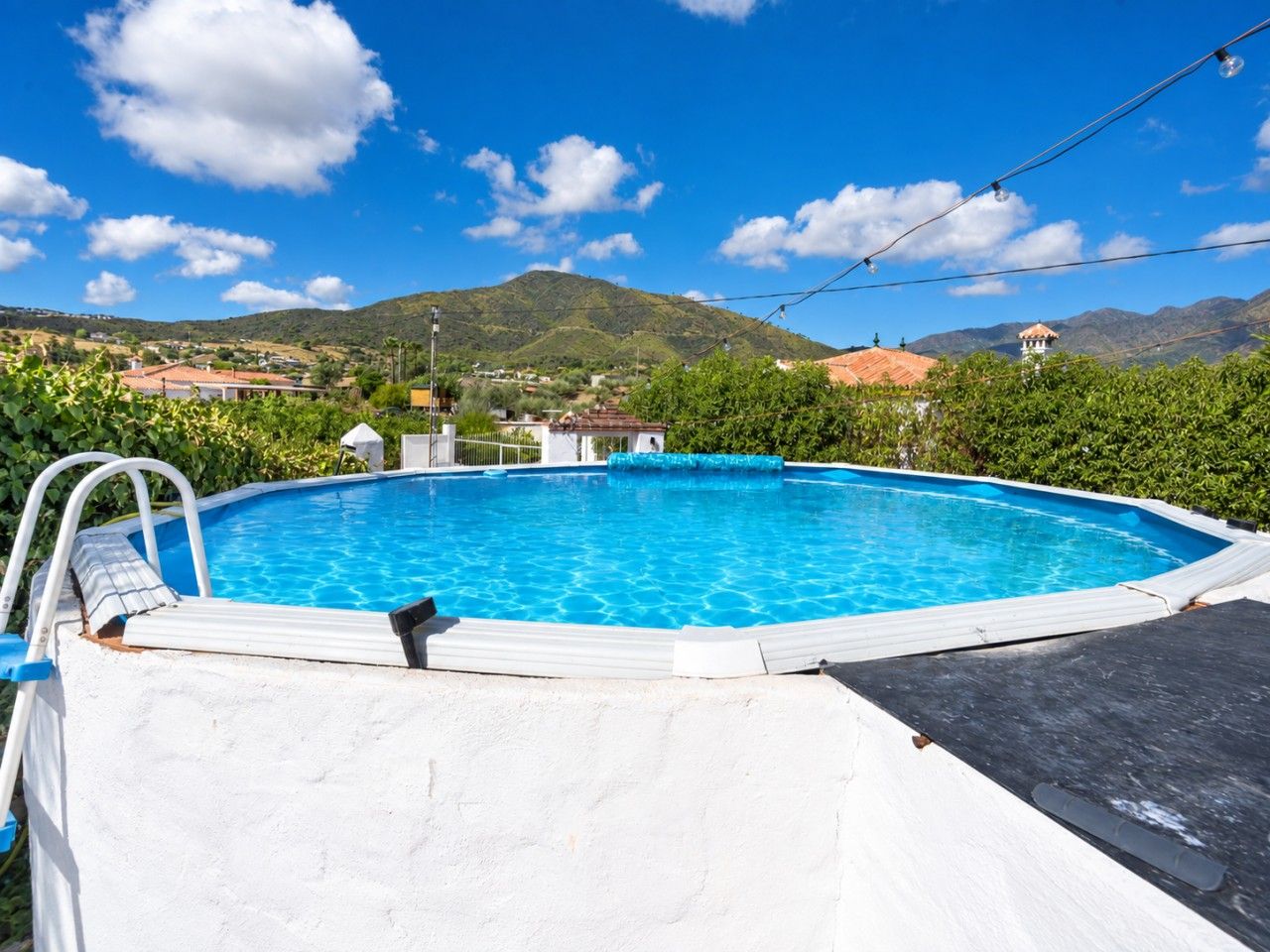 Una piscina con terraza blanca, rodeada de vegetación y un telón de fondo montañoso.