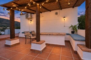 Um pátio externo com azulejos de terracota, pilares de madeira e luzes de corda.