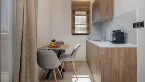 A compact kitchen with wooden cabinets, a marble countertop, and a dining area with chairs and a table.
