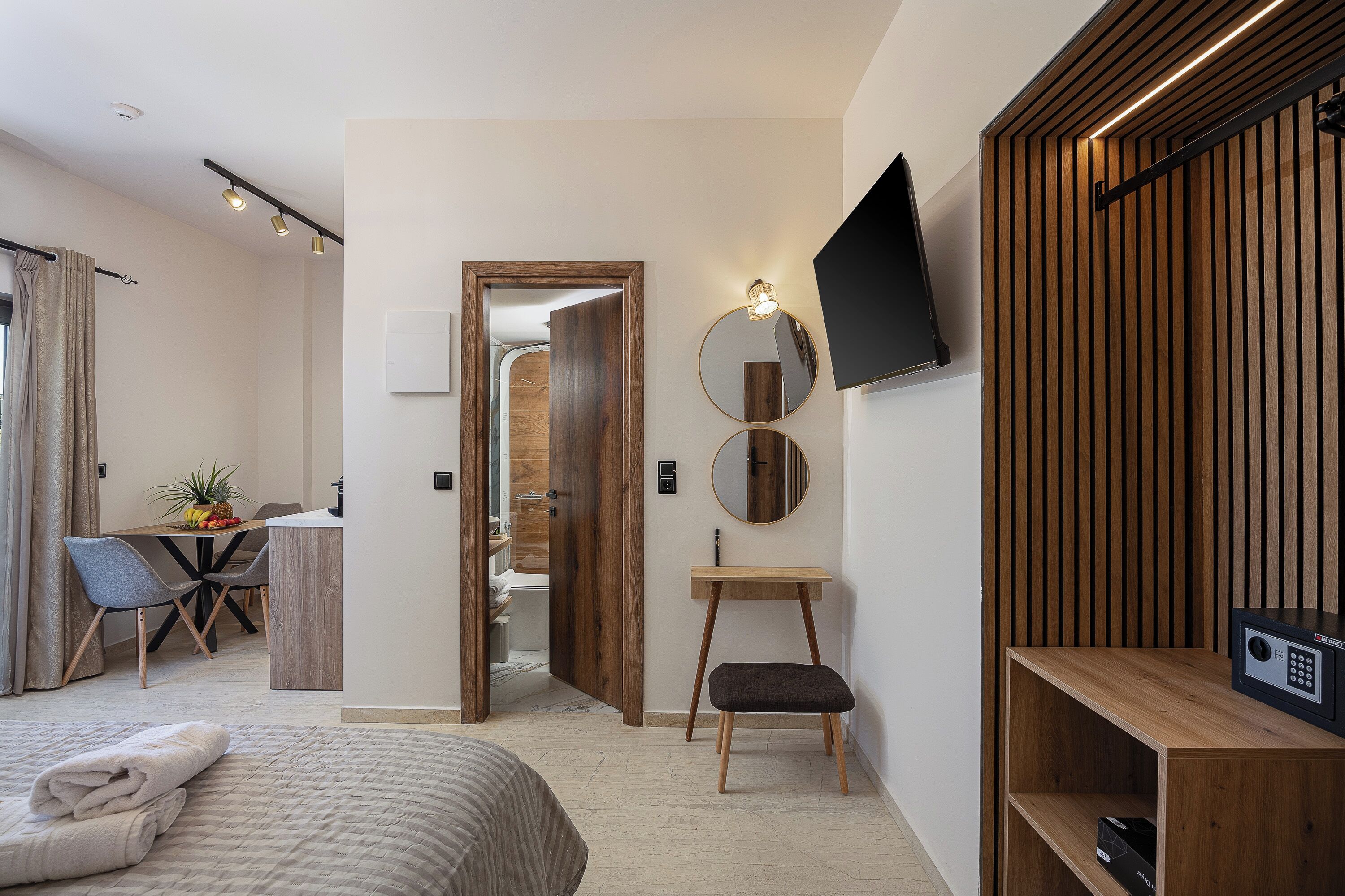 Une chambre d’hôtel moderne équipée d’un lit, d’un bureau, d’une chaise, d’un petit tabouret, d’un téléviseur fixé au mur et d’un panneau décoratif en bois sur le mur.