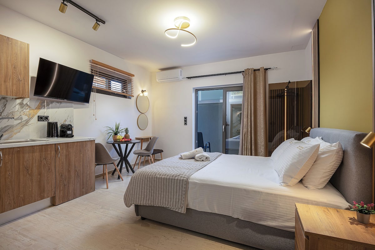A modern hotel room with a bed, bedside table, TV, and a small kitchenette.
