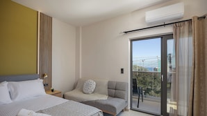 A modern hotel room with a bed, a sofa, a balcony with a view, and an air conditioning unit.
