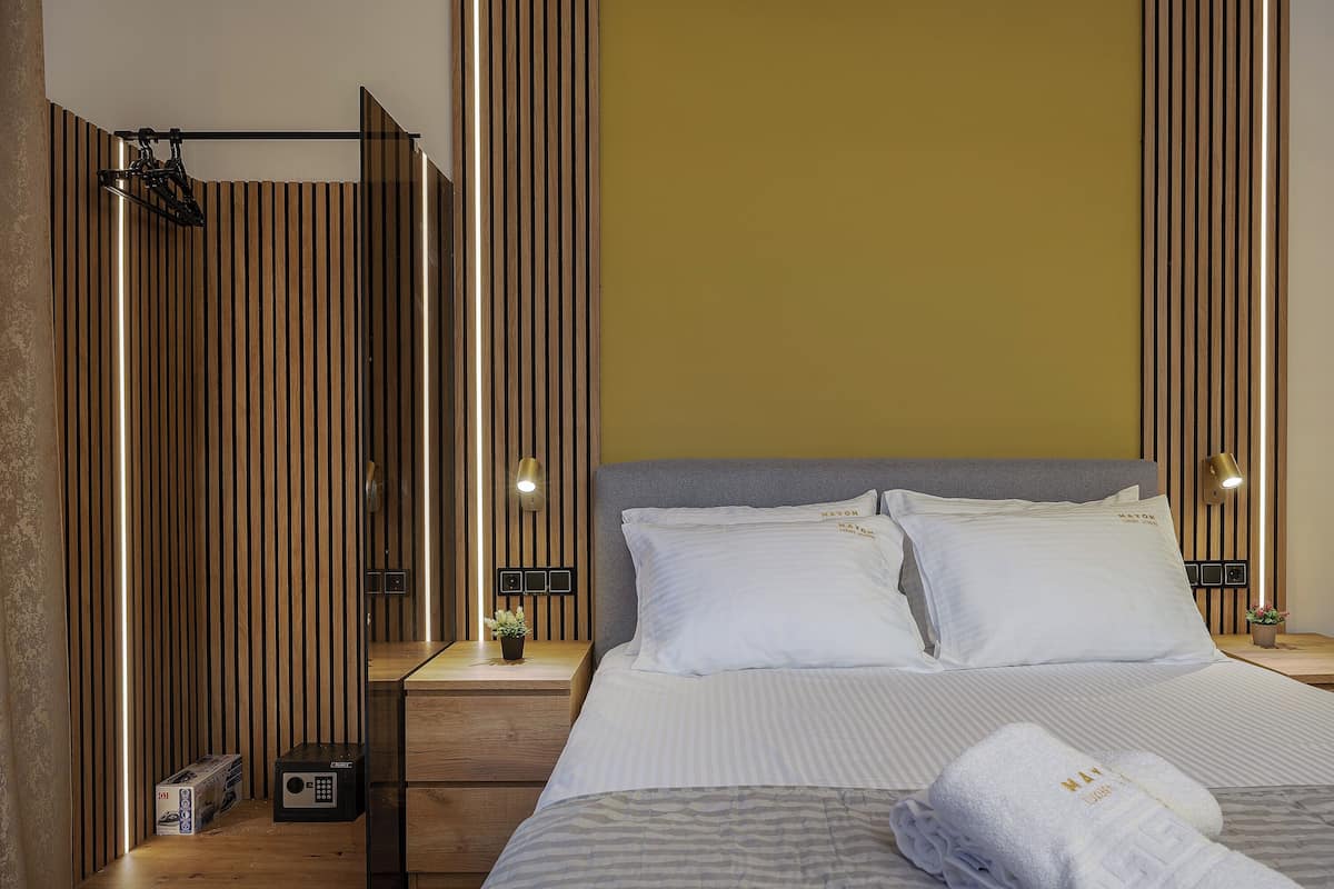 Une chambre d’hôtel comprenant un lit, des tables de chevet, une petite table, une lampe fixée au mur et un décor mural en panneaux de bois.