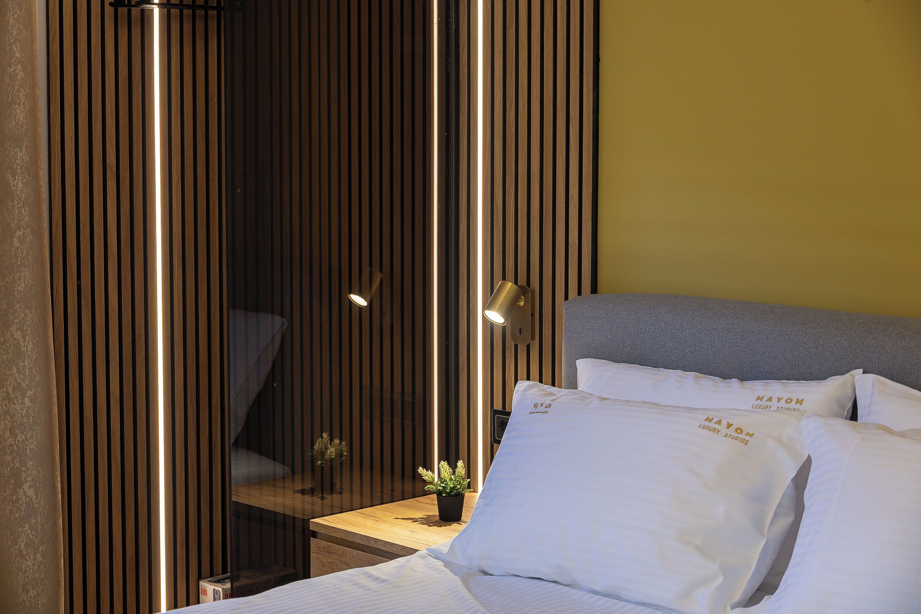 A hotel room with a bed, pillows, a small table with a plant, and a wooden partition with vertical slats.