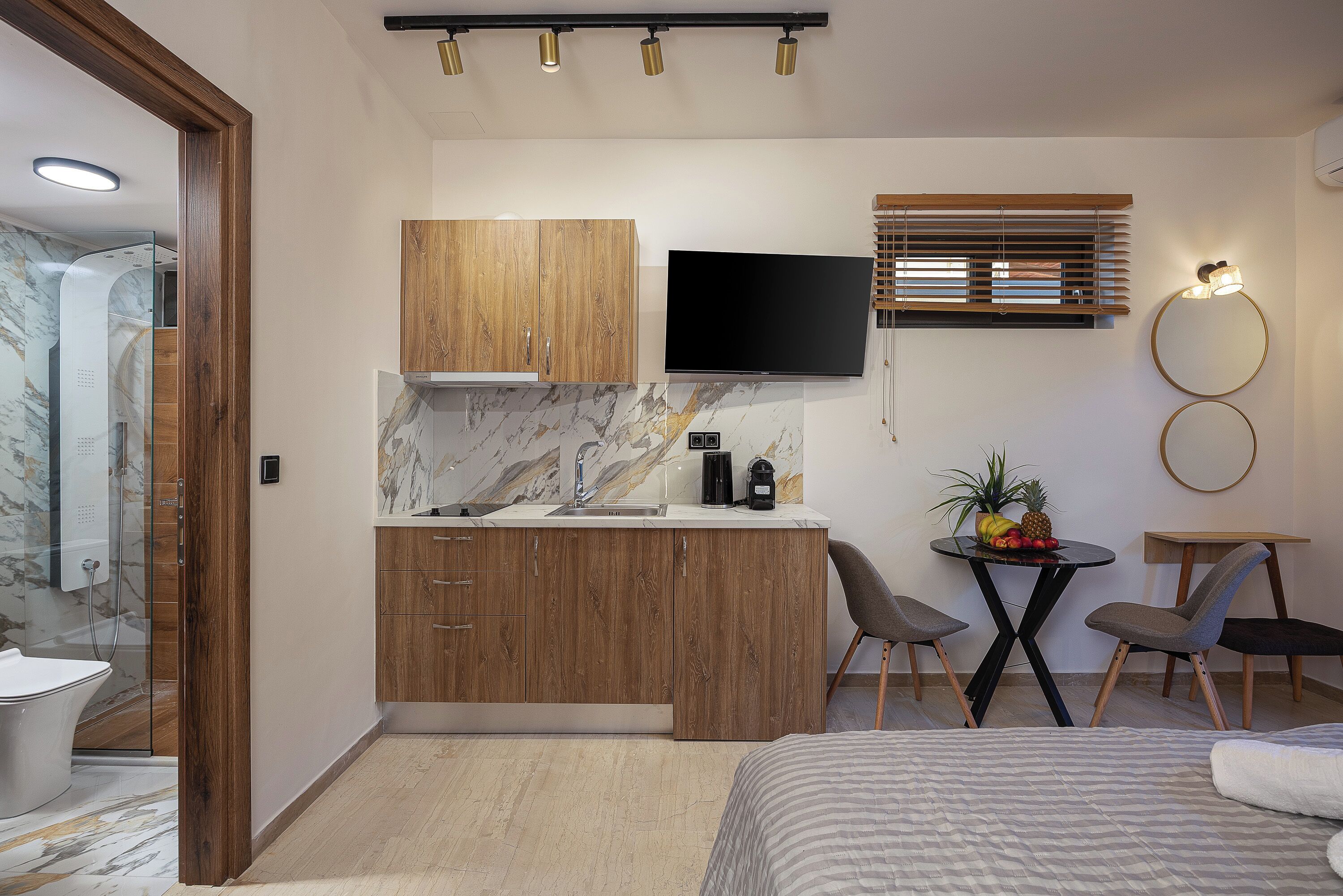 Een moderne keuken met houten kastjes, een flatscreen televisie en een klein eethoekje met stoelen en een tafel.