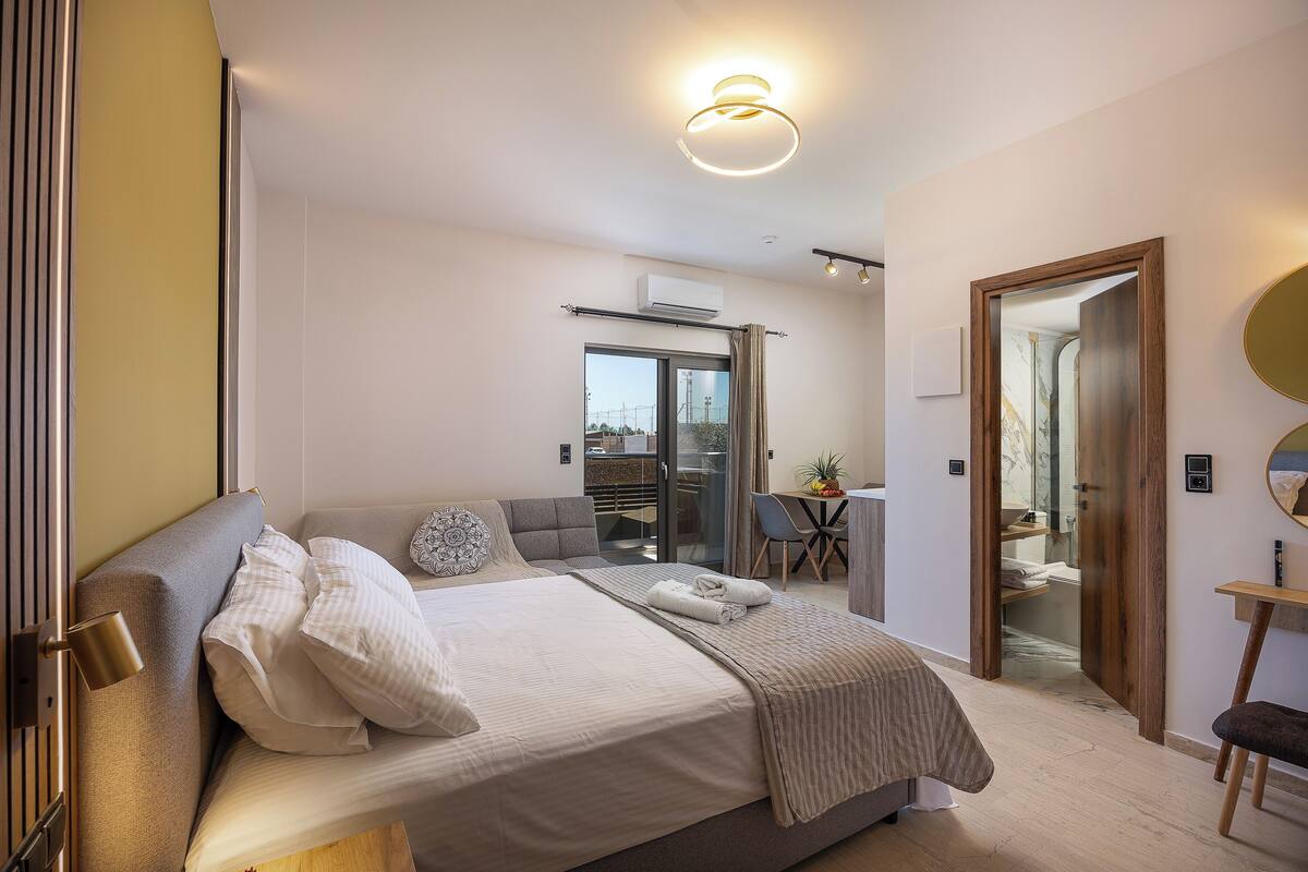 A modern hotel room with a large bed, a desk, and a view through a glass door.