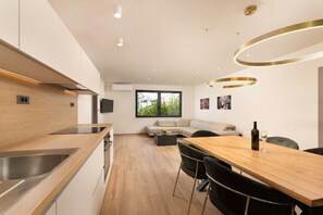 Eine moderne Küche mit Holzarbeitsplatte, ein Essbereich mit Holztisch und Stühlen, eine Couch und ein großes Fenster.