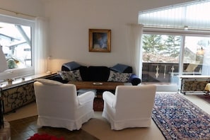 Ein Wohnzimmer mit einer Couch, zwei Sesseln, einem Gemälde an der Wand und einem großen Fenster mit Blick.