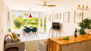 Eine moderne Küche mit einer Holzinsel, einem Essbereich mit Stühlen, einem Fernseher und Blick auf einen Garten.