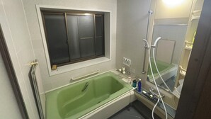 Une salle de bain avec une baignoire verte, une douche, des toilettes et une fenêtre située au-dessus de la baignoire.