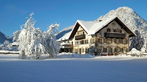 En snötäckt byggnad med en balkong, omgiven av snötäckta träd och berg.