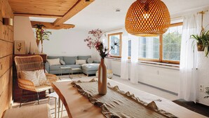 Ett modernt vardagsrum med ett träpanelat tak, en hängande lampa med flätad skärm, en soffgrupp, ett soffbord och en vas med blommor.