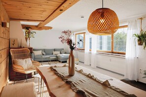 A modern living room with a wooden ceiling, a woven pendant light, a sofa set, a coffee table, and a vase with flowers. - Villa Senz - Bliss (Pfronten)
