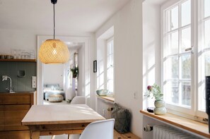 A kitchen with a wooden table, white chairs, a hanging light fixture, and a window with a view. - Villa Senz - Bliss (Pfronten)