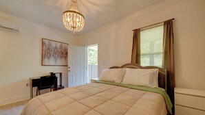 A bedroom with a bed, a desk, a chair, a chandelier, a window with curtains, and a door. - Walk Downtown! Hinton Historic District Studio (Hinton)