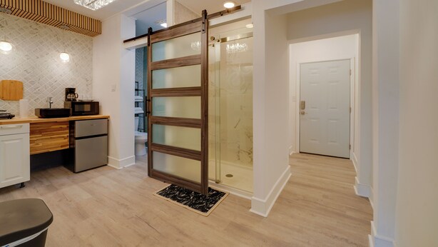 A modern kitchen with a coffee maker, a refrigerator, and a sliding glass door leading to a shower area. - Walk Downtown! Hinton Historic District Studio (Hinton)