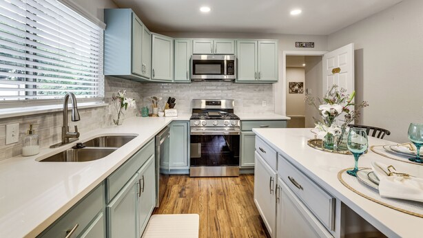 Una cocina con armarios azul claro, un microondas de acero inoxidable y una estufa.