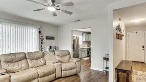Una sala de estar con un sofá seccional color beige, un ventilador de techo y una mesa de comedor con alfombra.
