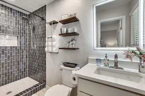 Ein modernes Badezimmer mit Dusche, Toilette und Waschbecken, mit einer gefliesten Rückwand und dekorativen Regalen.