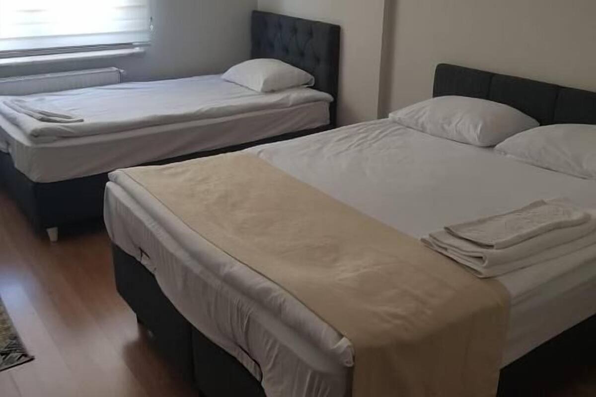 A room with two beds, a window with blinds, and a wooden floor.