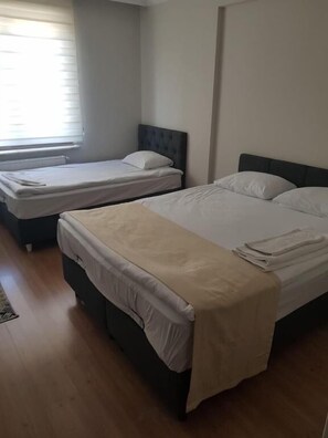 Ein Zimmer mit zwei Betten, einem Fenster mit Jalousien und Holzboden.