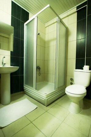 Een badkamer met douche, toilet, wastafel en spiegel.