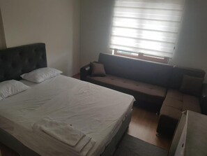 Ein Schlafzimmer mit Bett, Sofa, Fenster mit Jalousien und Koffer.