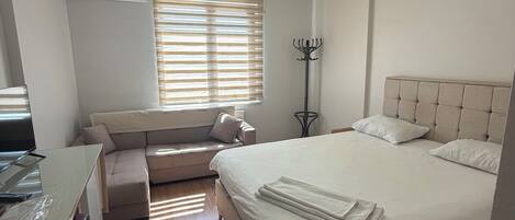 A bedroom with a bed, a desk, a chair, a window with blinds, and an air conditioning unit.