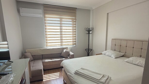 Un dormitorio con cama, escritorio, silla, perchero y ventana con persianas.