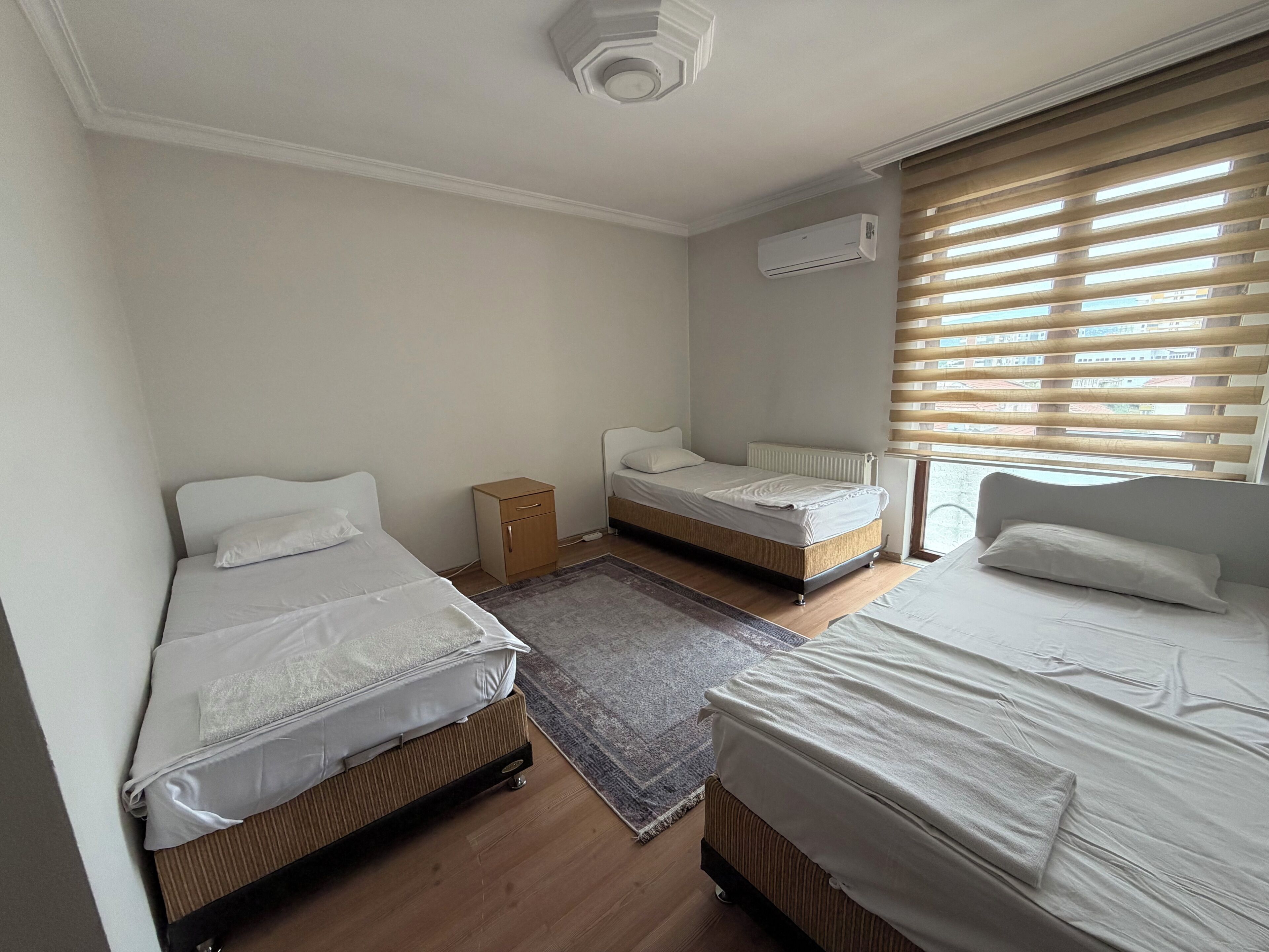 A hotel room with two single beds, a small wooden cabinet, a radiator, and a window with blinds.