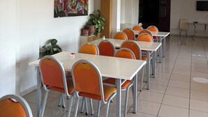 Un comedor con varias mesas y sillas, un techo con diseño de cuadrícula, un cuadro colgado en la pared y una planta en maceta.