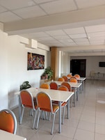 Un comedor con varias mesas y sillas, un techo con diseño de cuadrícula, un cuadro colgado en la pared y una planta en maceta.