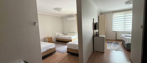 A bedroom with two beds, a small table, a radiator, and a window with blinds.