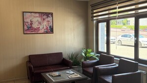 Una habitación con un sofá de cuero marrón, una mesa de centro de cristal, un cuadro en la pared y una ventana con persianas.