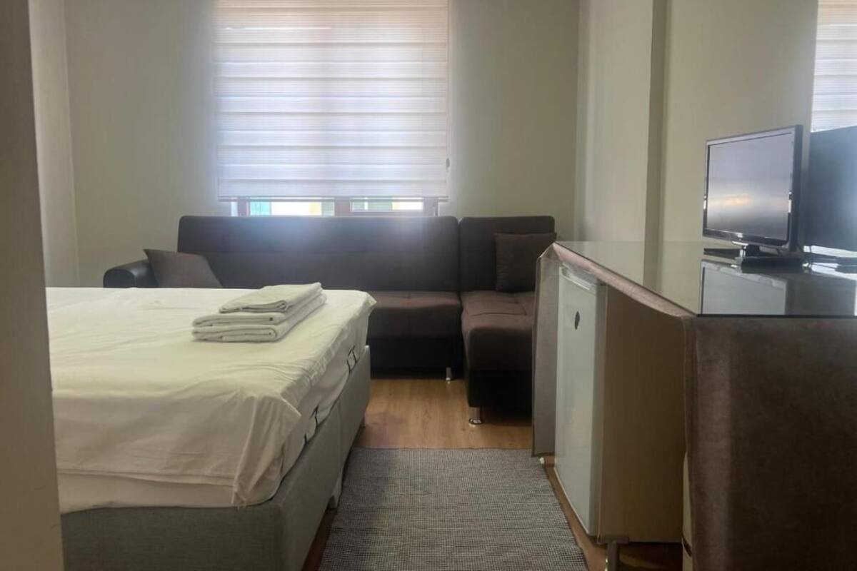A compact room with a bed, a sofa, a television, and a small refrigerator.
