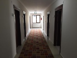A hallway with patterned flooring, doors on both sides, and a window at the end. - korkmaz rezidans  (melikgazi)