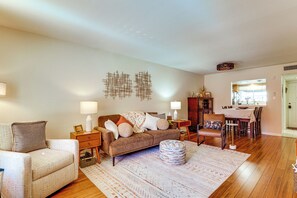 A living room with a sofa, ottoman, and a dining area with chairs and a table. - Steps to Fashion Square! Condo w/ Patio & Pool (Scottsdale)