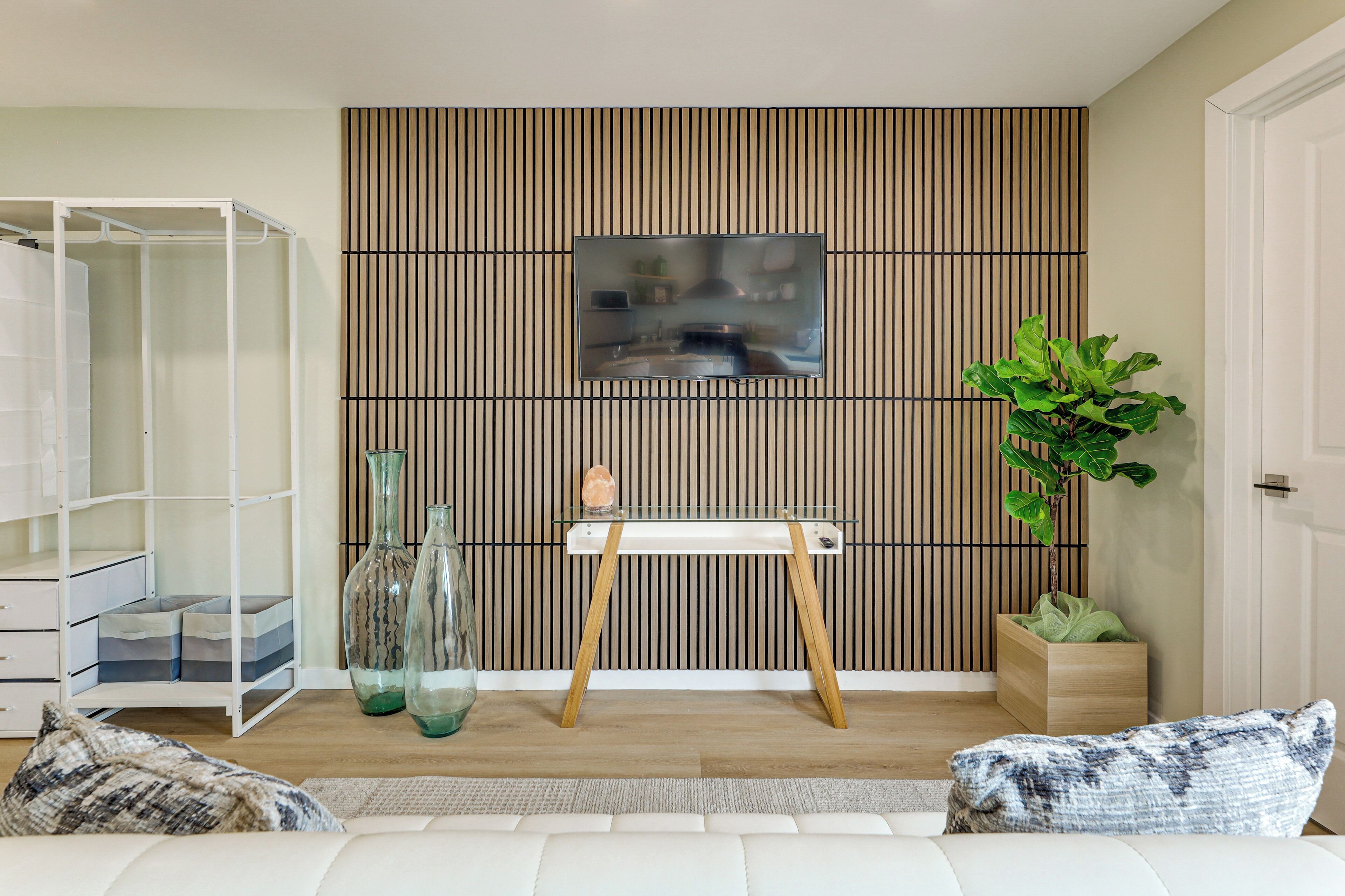 A modern living room with a white sofa, a glass coffee table, a wooden cabinet, a potted plant, and a wall-mounted TV.