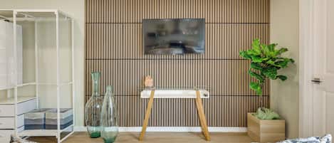 A modern living room with a white sofa, a glass coffee table, a wooden cabinet, a potted plant, and a wall-mounted TV.