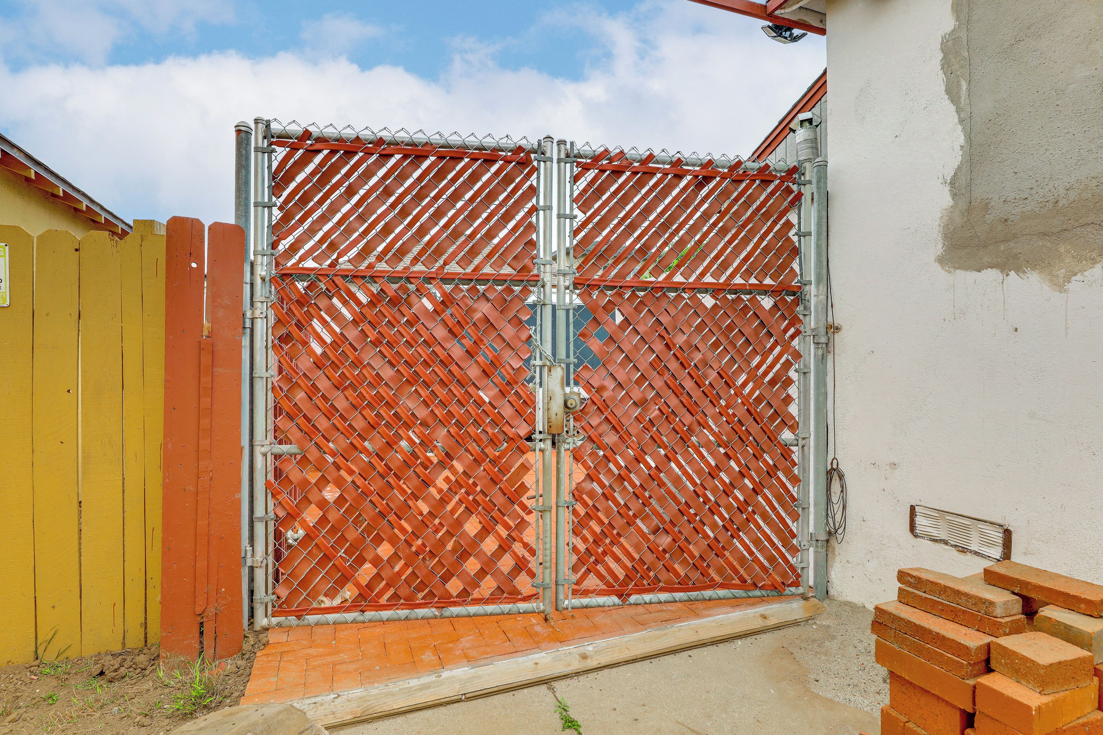 Un espace délimité par une clôture en métal, une clôture jaune et orange, et une pile de briques.