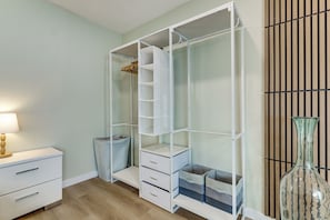 Una habitación con un armario blanco, una mesita de noche con lámpara y un jarrón grande.