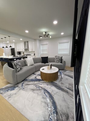 A modern living room with a sectional sofa, a round coffee table, and a kitchen in the background.