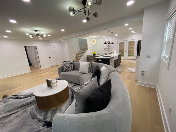 A modern living room with a grey sofa, a coffee table, and a staircase leading to a kitchen area.