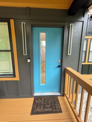 A blue door with a doormat, a window, and a wooden railing.