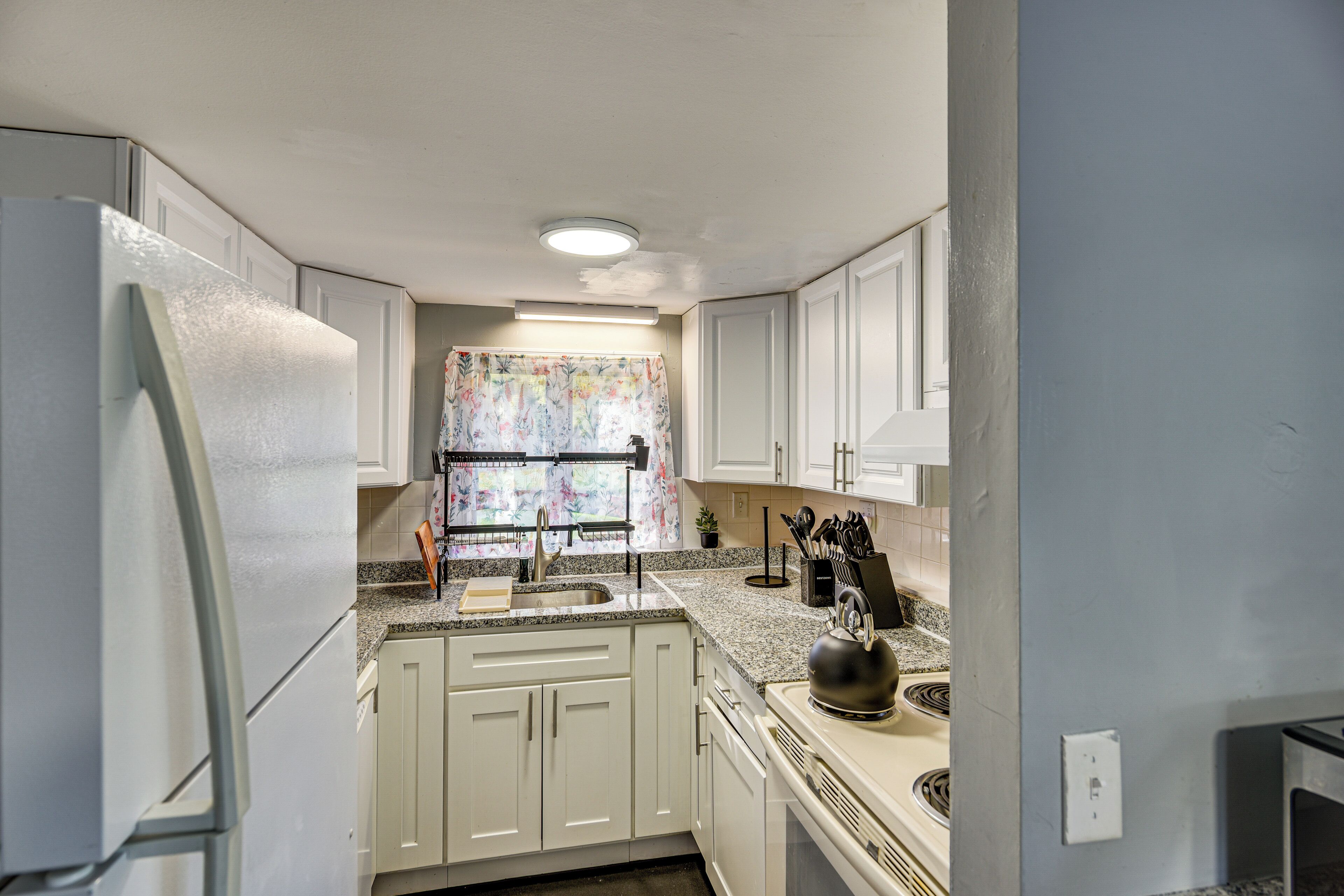 A kitchen with white cabinets, a stainless steel refrigerator, a sink, and a kettle on the counter.